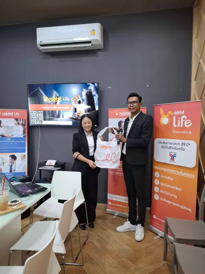 ตัวแทนสองคนในชุดสูท ยืนหน้าจอนำเสนอข้อมูลบริษัทแรบบิท ไลฟ์