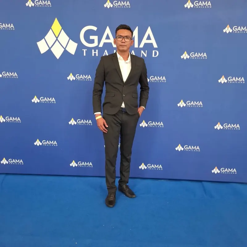 ตัวแทนในชุดสูทสีดำ ยืนหน้าฉากงาน GAMA Thailand